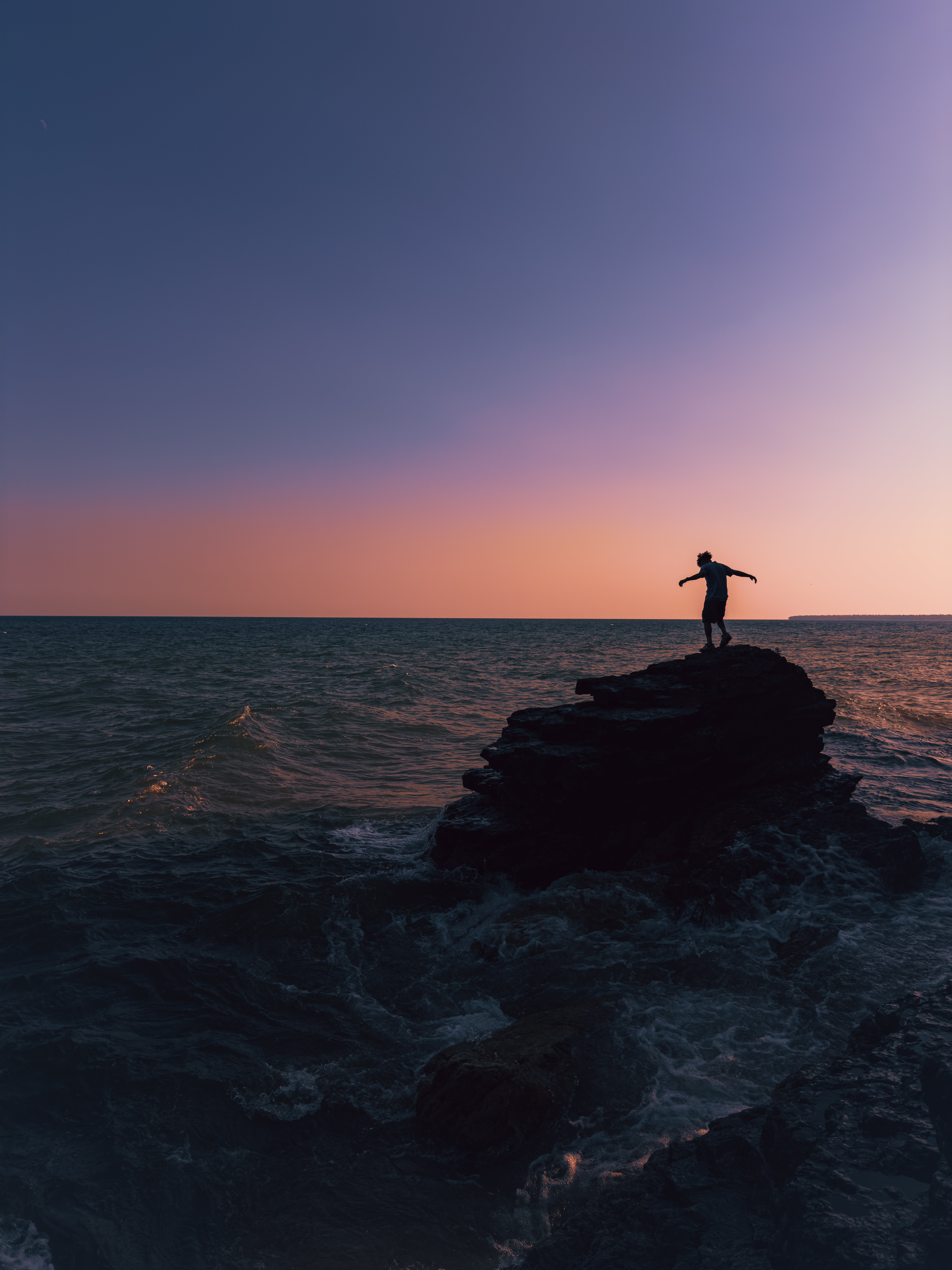 Silhouette on rock over water at sunset with purple-orange sky